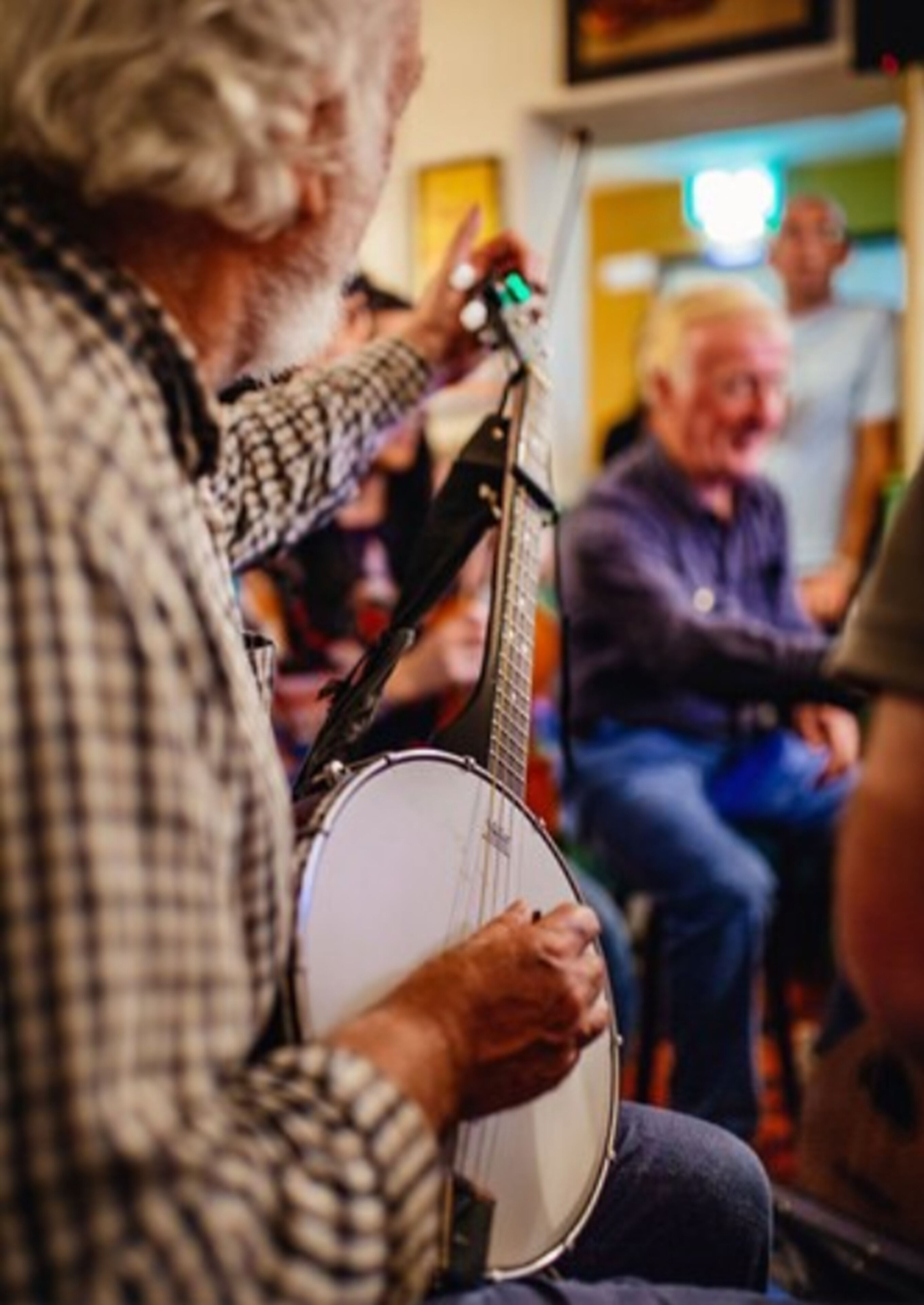 A person playing a banjo in a room with other people seated.