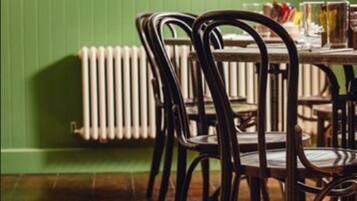 A dining area with wooden chairs and a table, a radiator, and framed pictures on the wall.