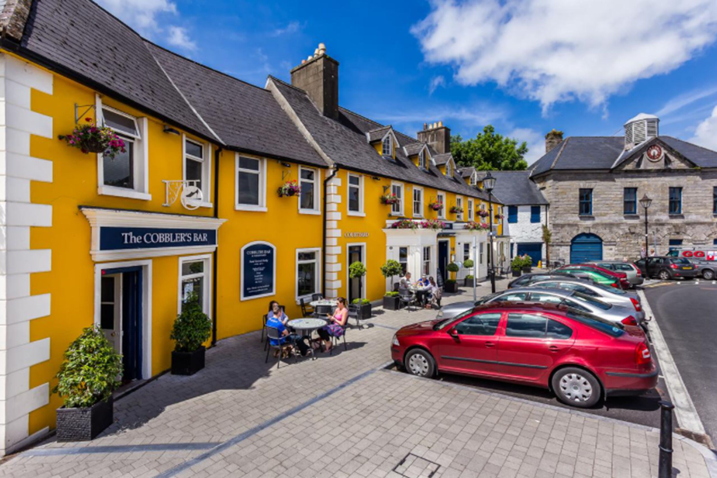 Un bâtiment jaune avec une enseigne indiquant « The Cobble's Bar » et une voiture rouge garée devant.