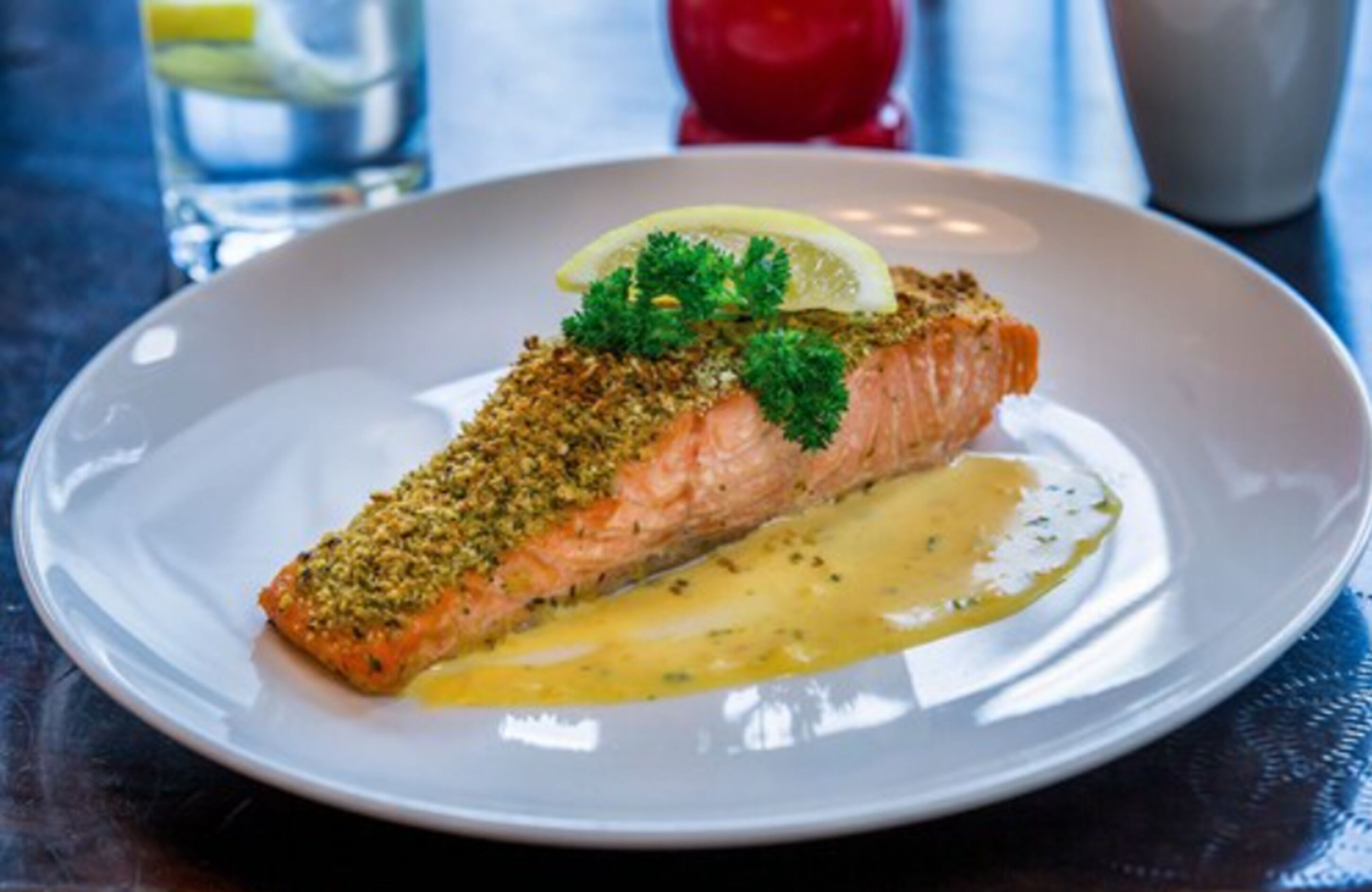 A plate with a piece of salmon topped with herbs and a lemon slice, served on a white plate.