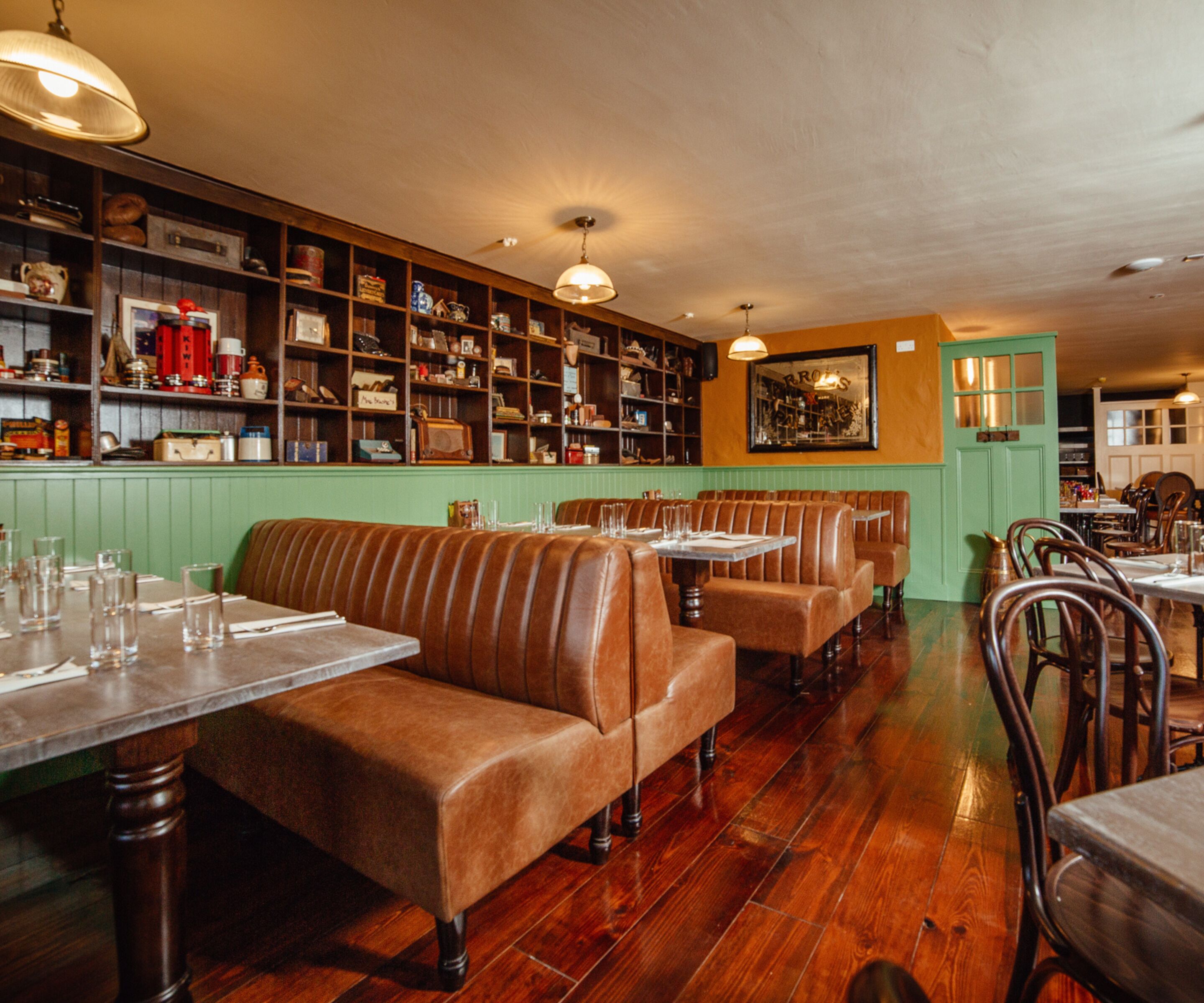 Interior de restaurante con cabinas de madera, una pared verde y estanterías con diversos objetos.