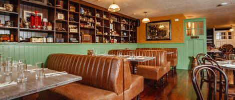 Interior de restaurante con cabinas de madera, una pared verde y estanterías con diversos objetos.