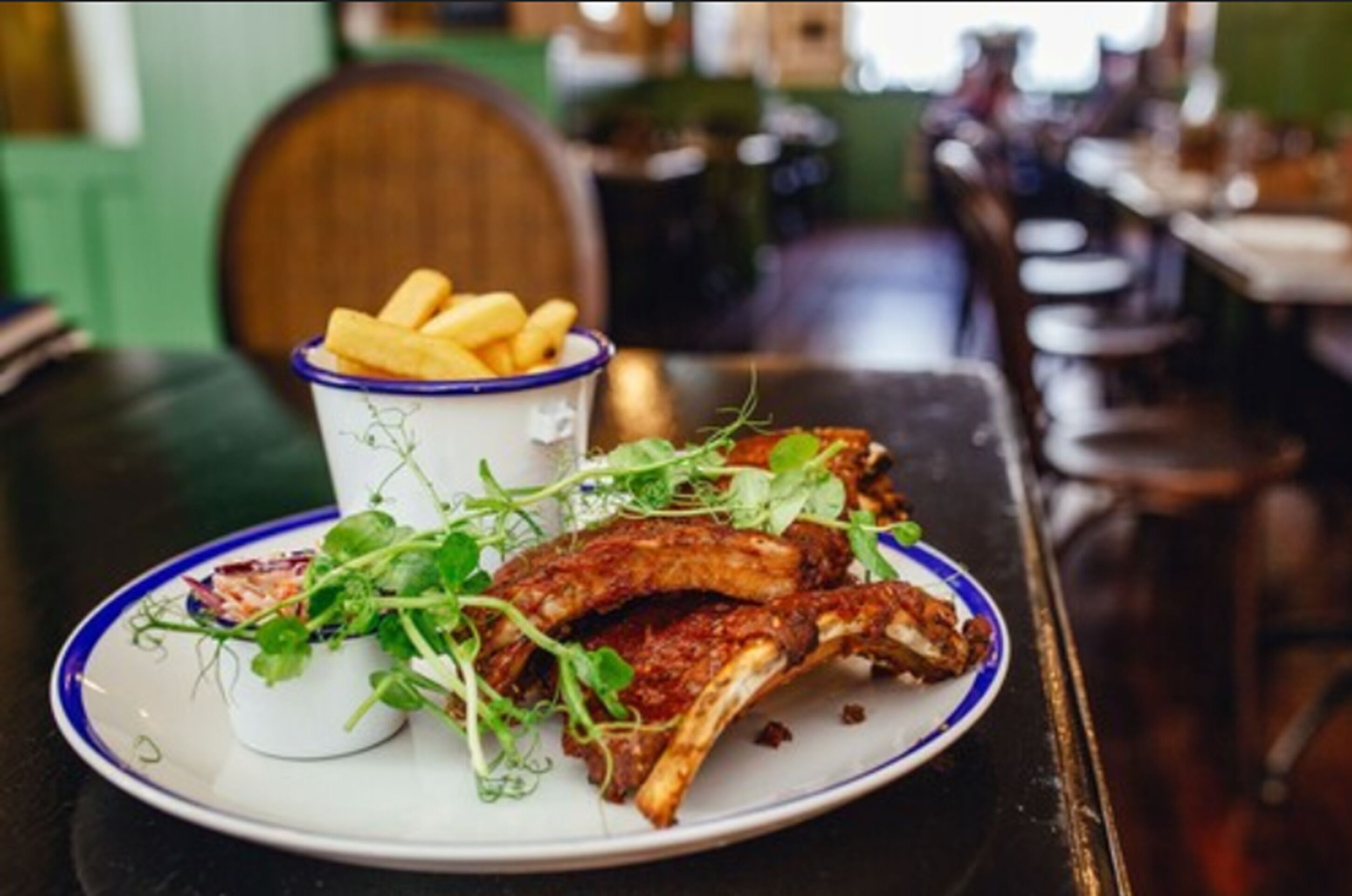 Un plato de costillas y papas fritas, y una taza de papas fritas.