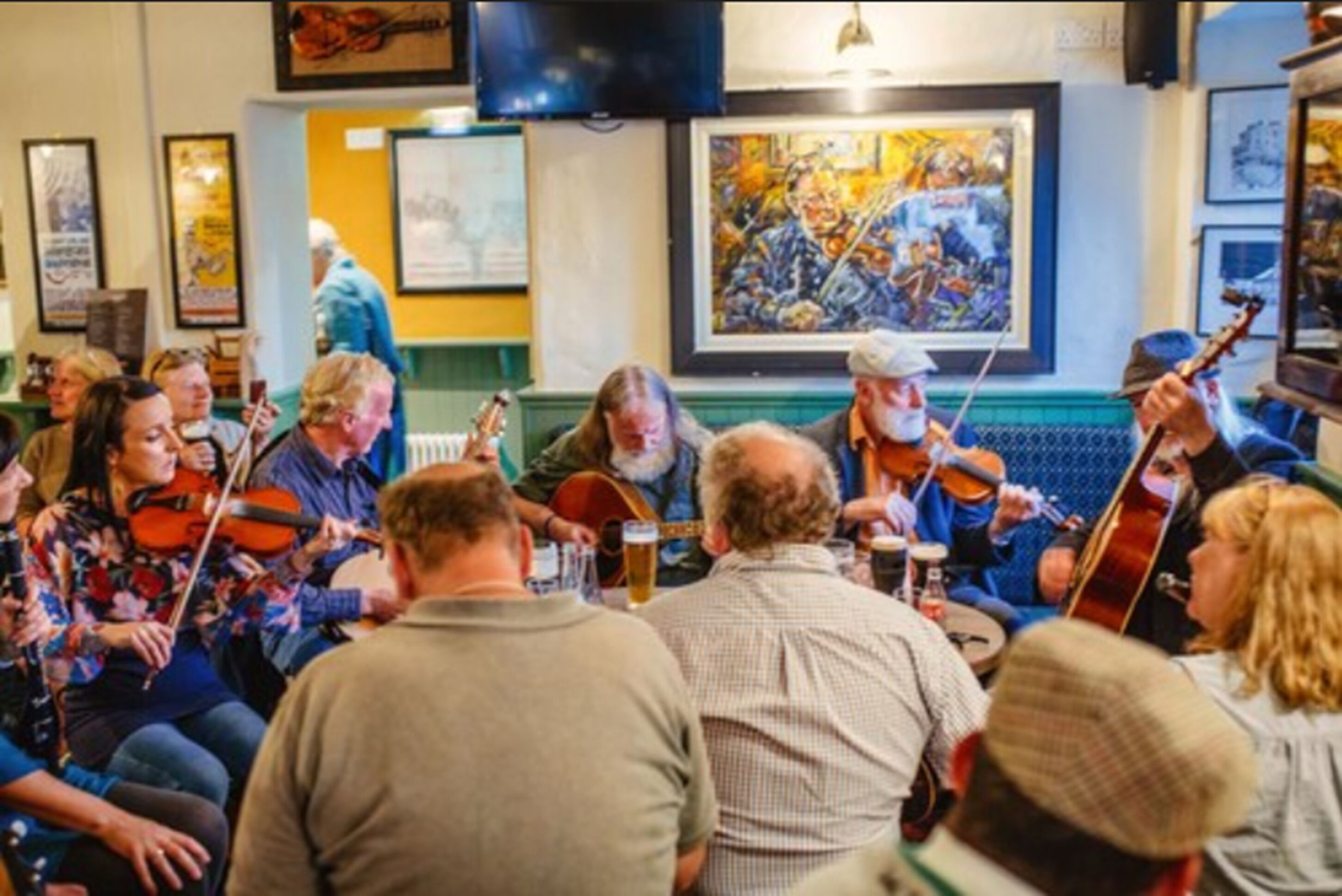 A group of people seated around a table, engaged in playing string instruments.