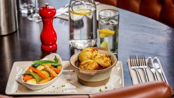 A dining table with a plate of food, a bottle of water, a glass of water, a red pepper shaker, and cutlery.