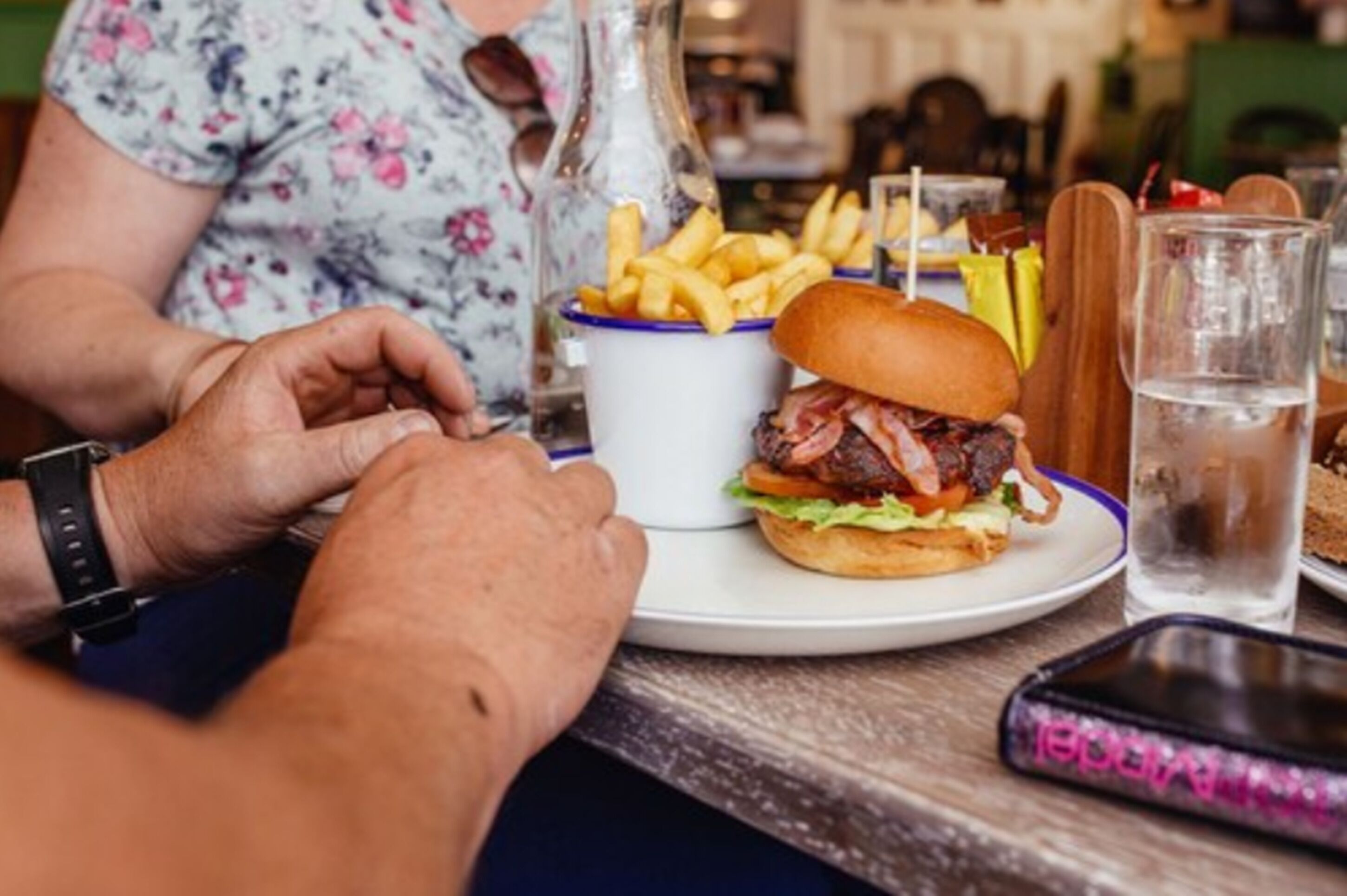Una persona sentada a una mesa con una hamburguesa, papas fritas y una bebida.