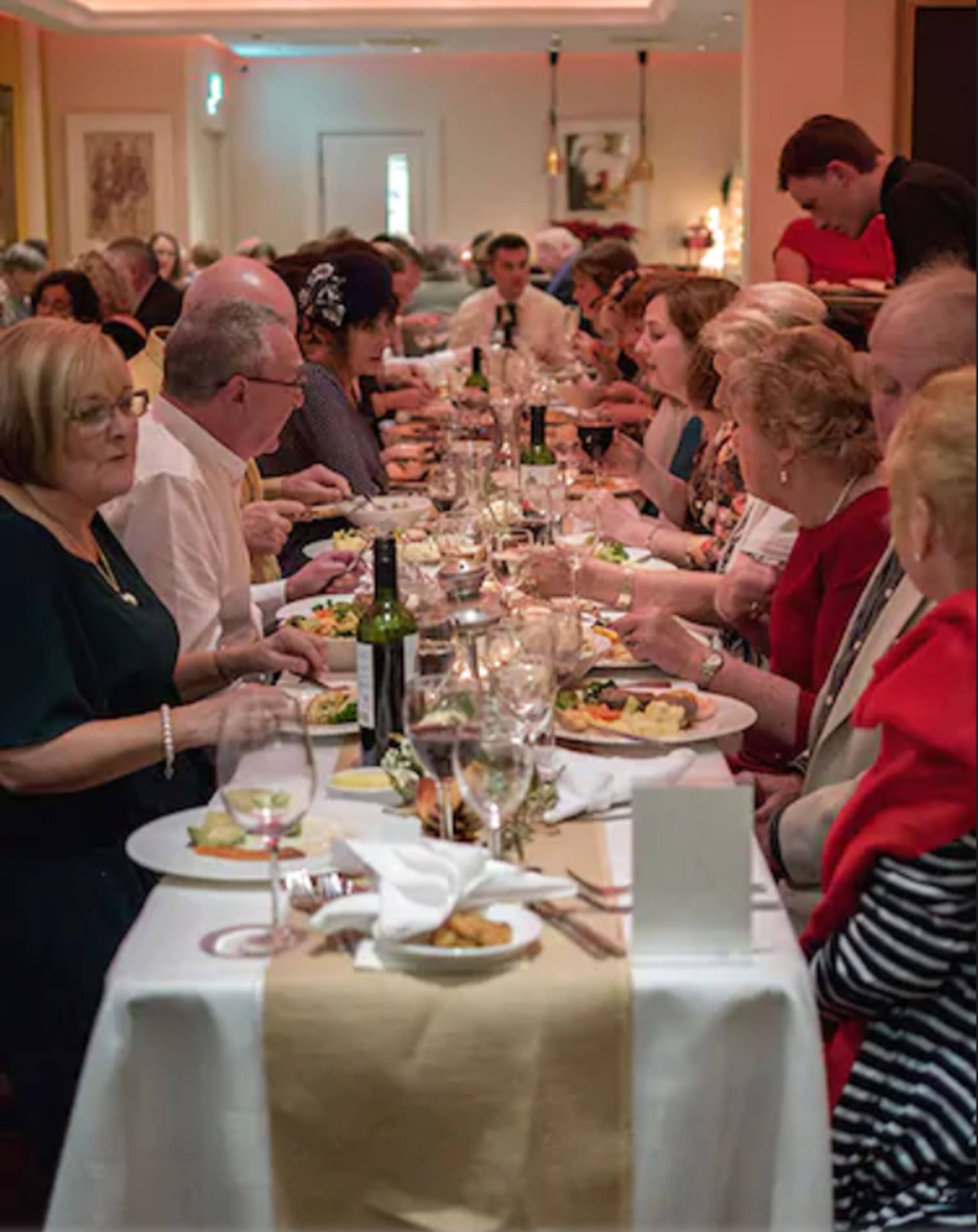 Una larga mesa de comedor con varias personas sentadas, conversando y comiendo.