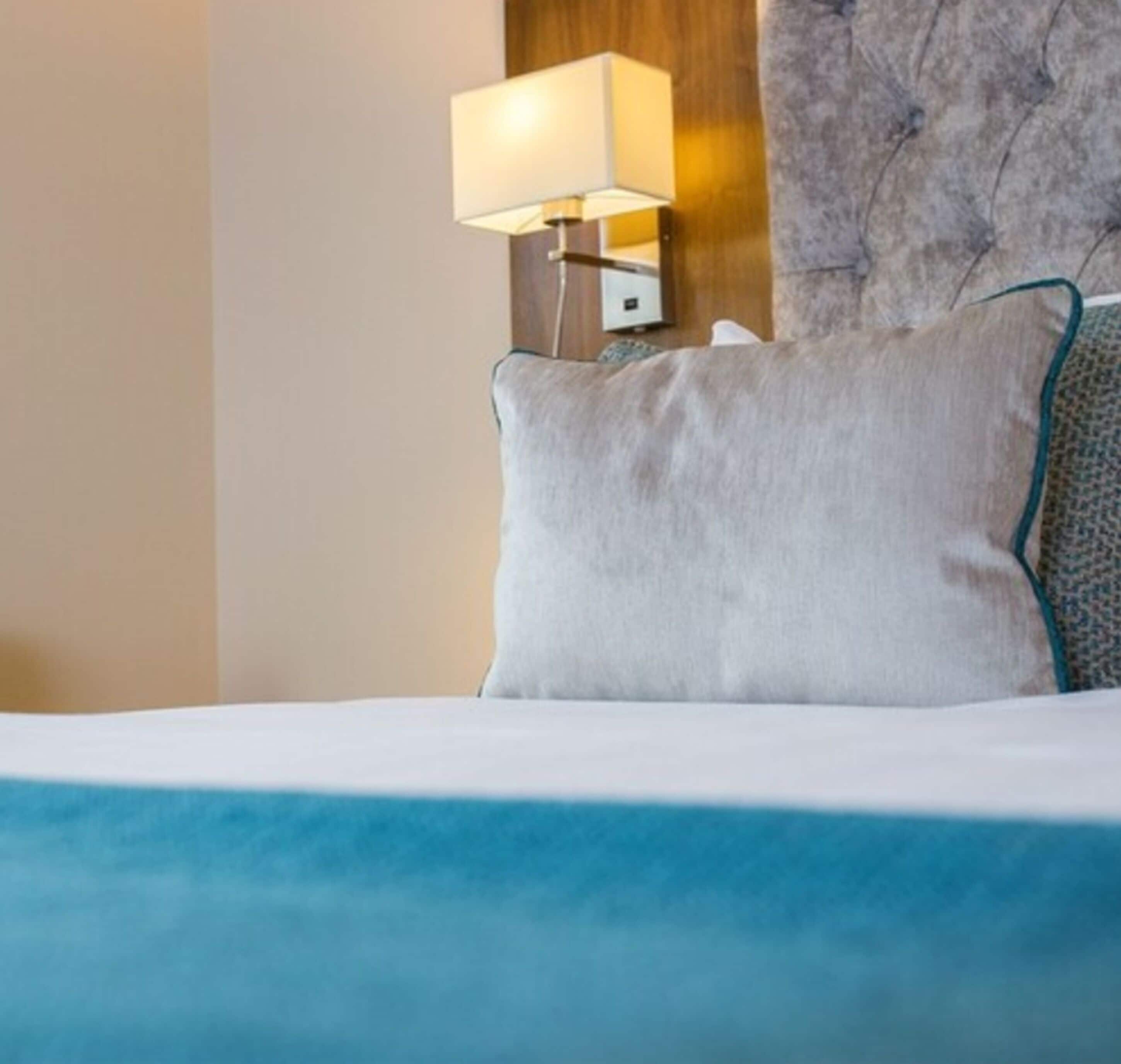 Una cama bien hecha con un almohadón blanco y una manta azul.