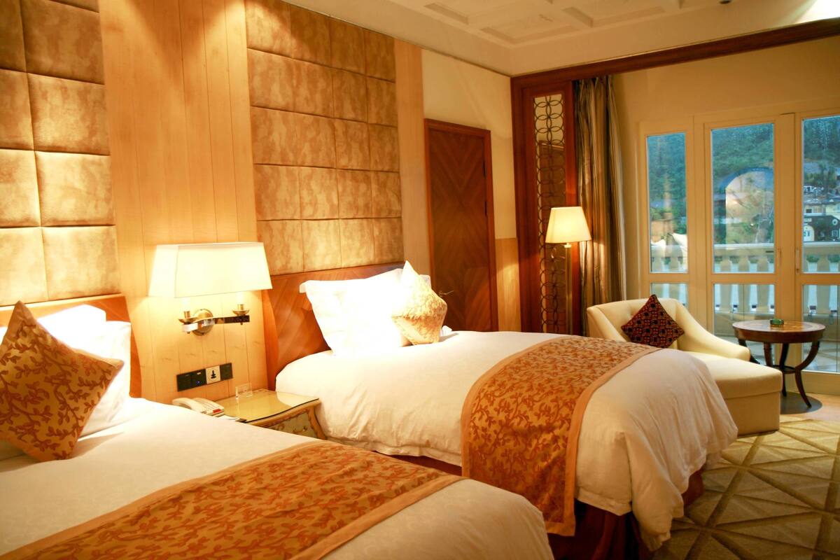 Een hotelkamer met twee bedden, een zithoek met een stoel en een tafeltje, en een groot raam met uitzicht op de omgeving.