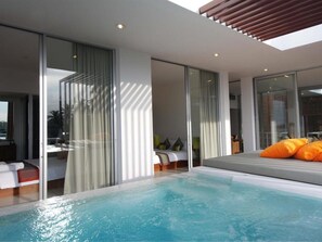 Habitación de hotel moderna con un amplio ventanal que da a un balcón, un jacuzzi exterior privado y una cama con almohadas naranjas.