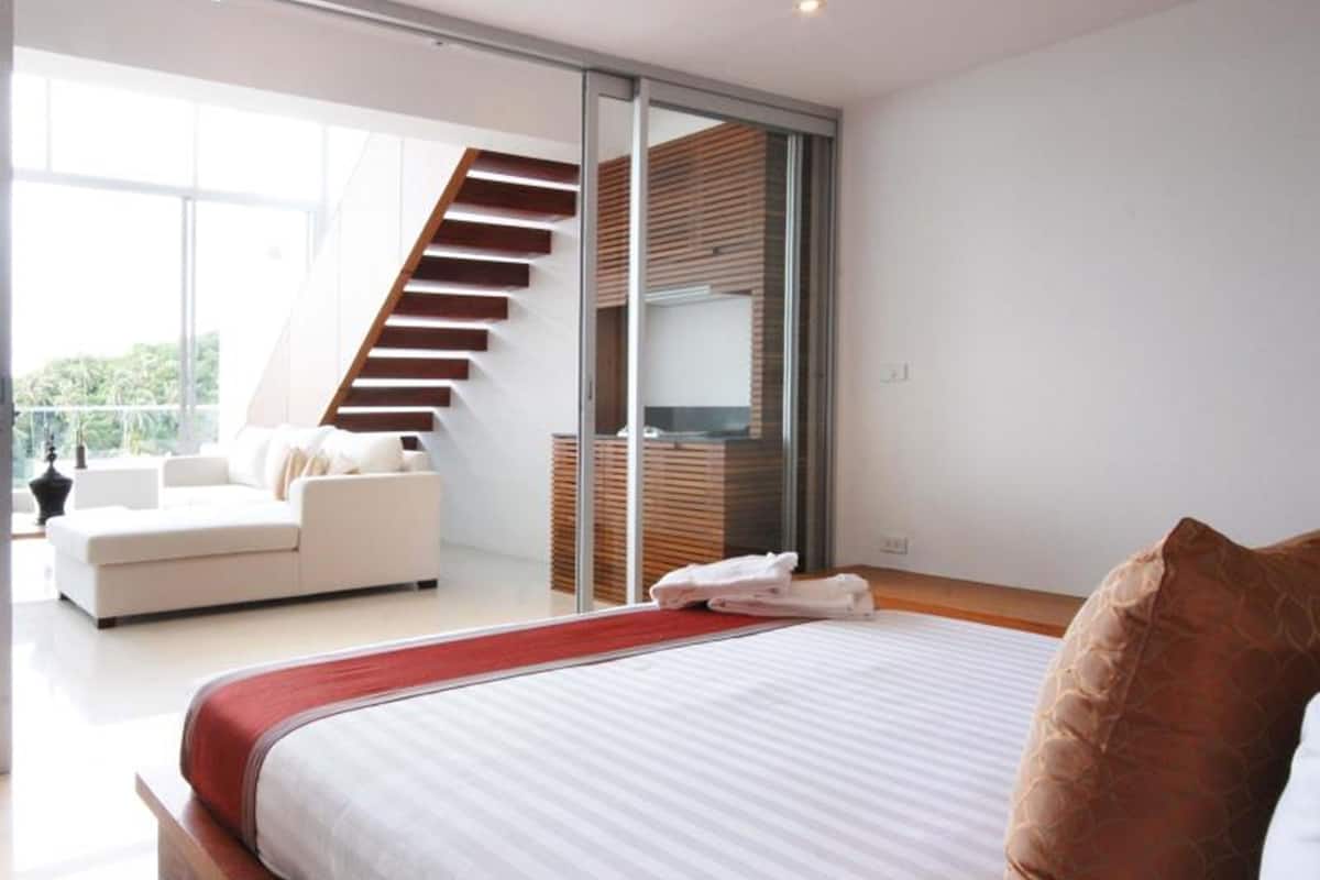Un dormitorio moderno con una cama grande, una escalera que conduce a un nivel superior y vistas de follaje en el exterior.