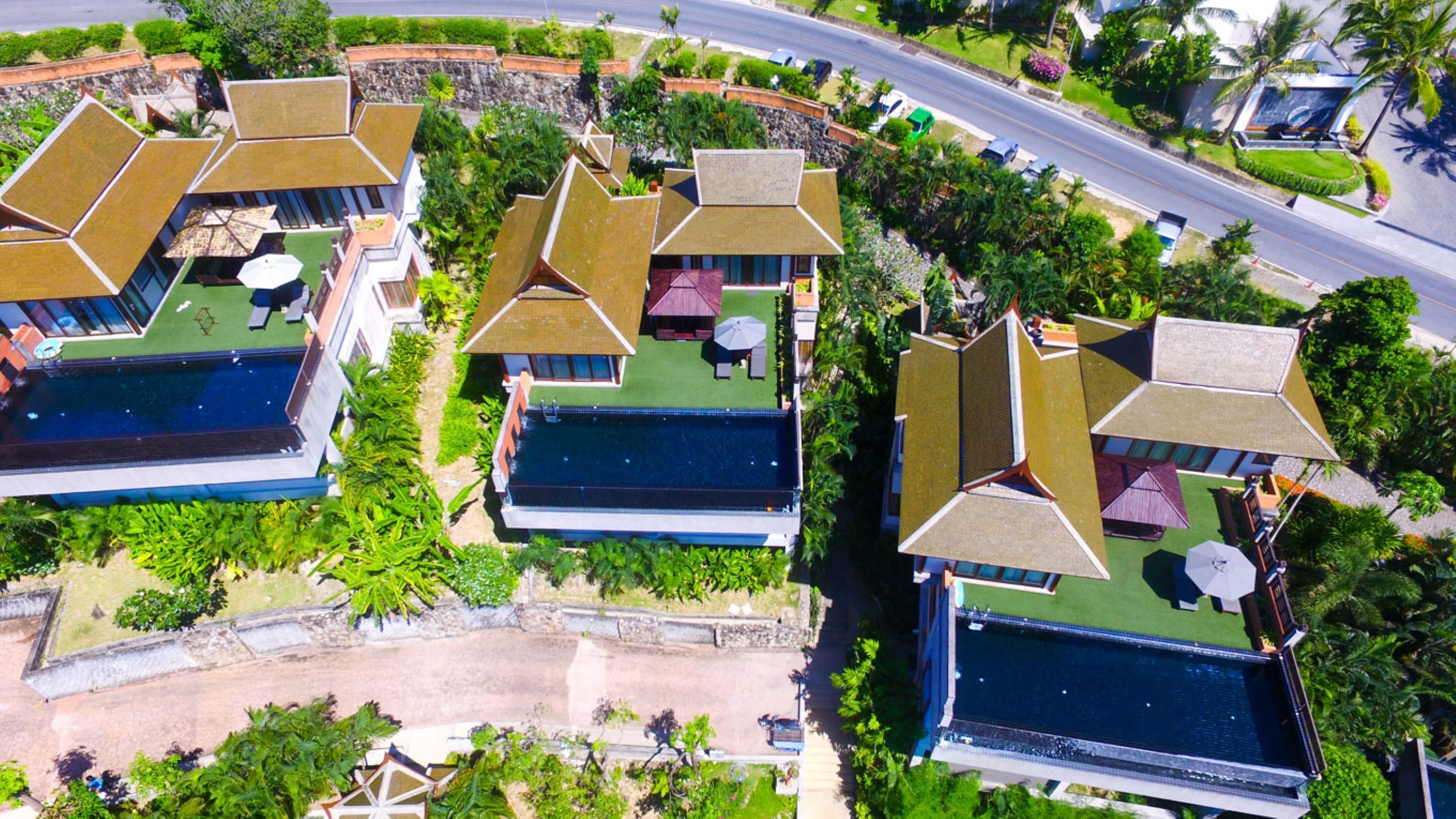 An aerial view of a resort with multiple buildings, each featuring a swimming pool and surrounded by lush greenery.