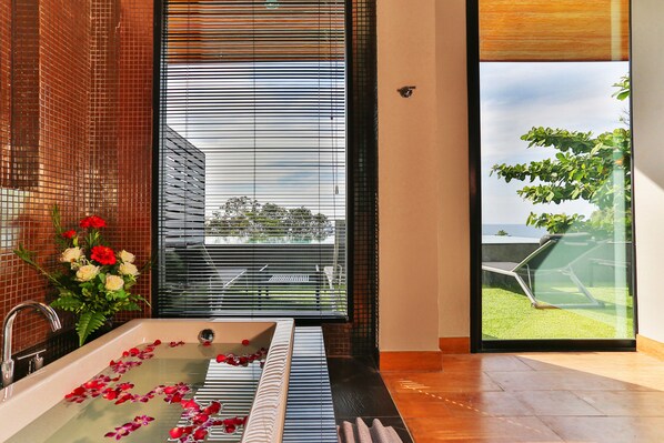 Un baño moderno con bañera, una ventana con persianas y vista a un jardín.