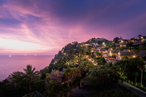 Un resort costero con varias edificaciones, abundante vegetación y vista al mar al atardecer.