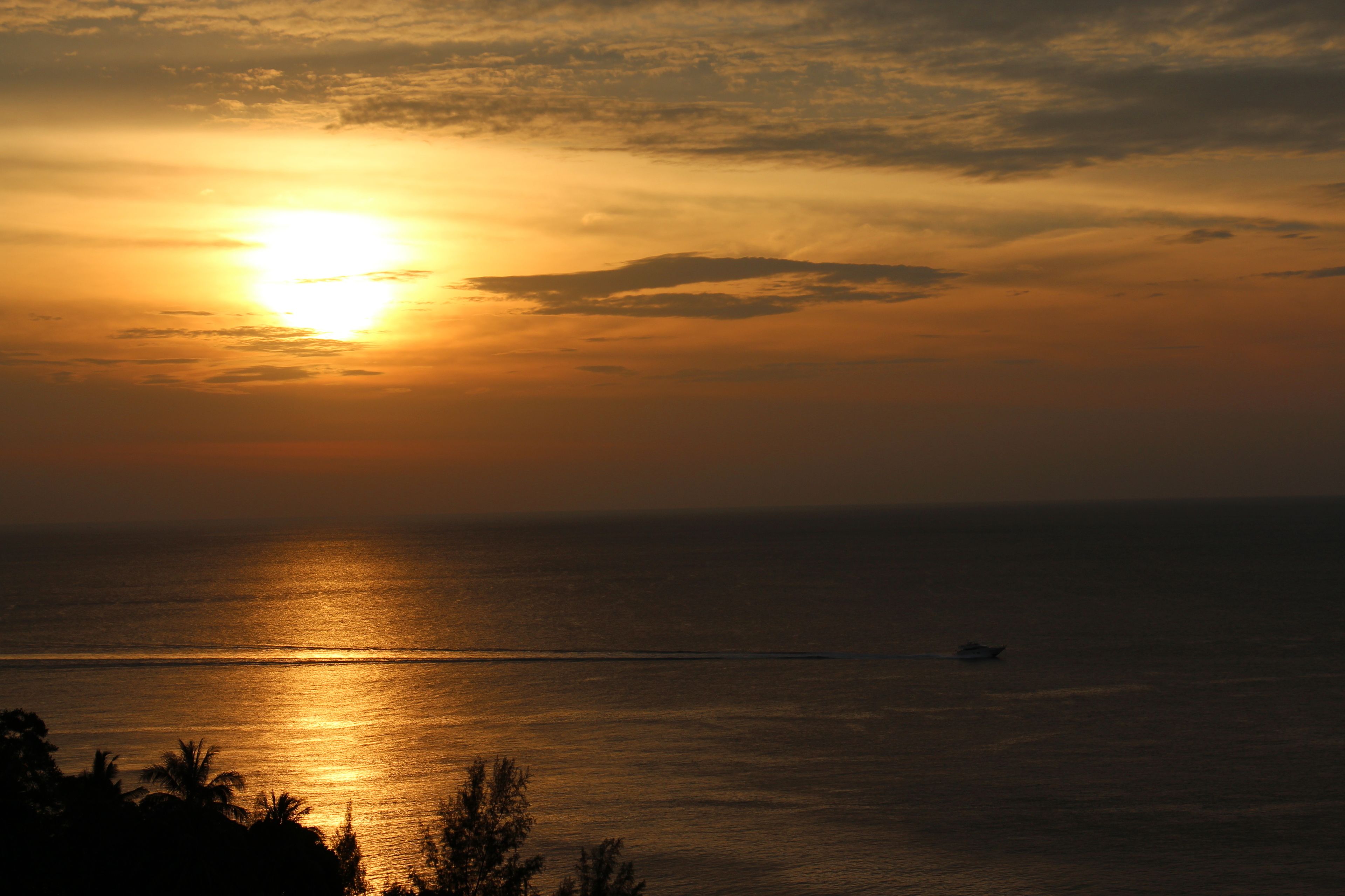 A sunset over a calm sea with a boat in the distance.
