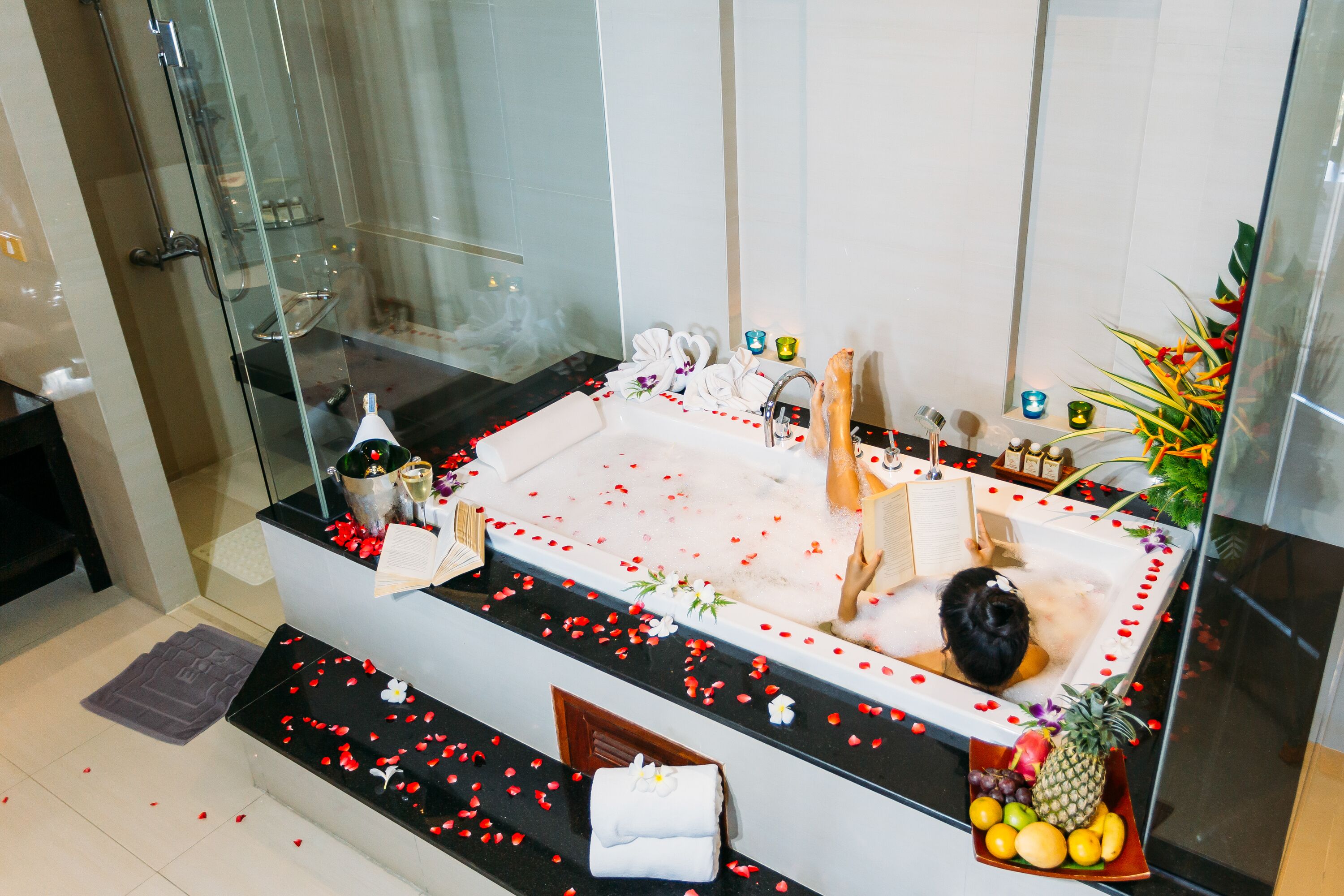 Une salle de bain moderne avec une grande baignoire, une cabine de douche en verre et un panier de fruits posé sur le côté.