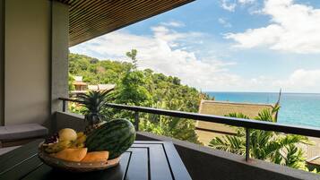 A balcony with a fruit bowl, a view of the ocean, and lush greenery.