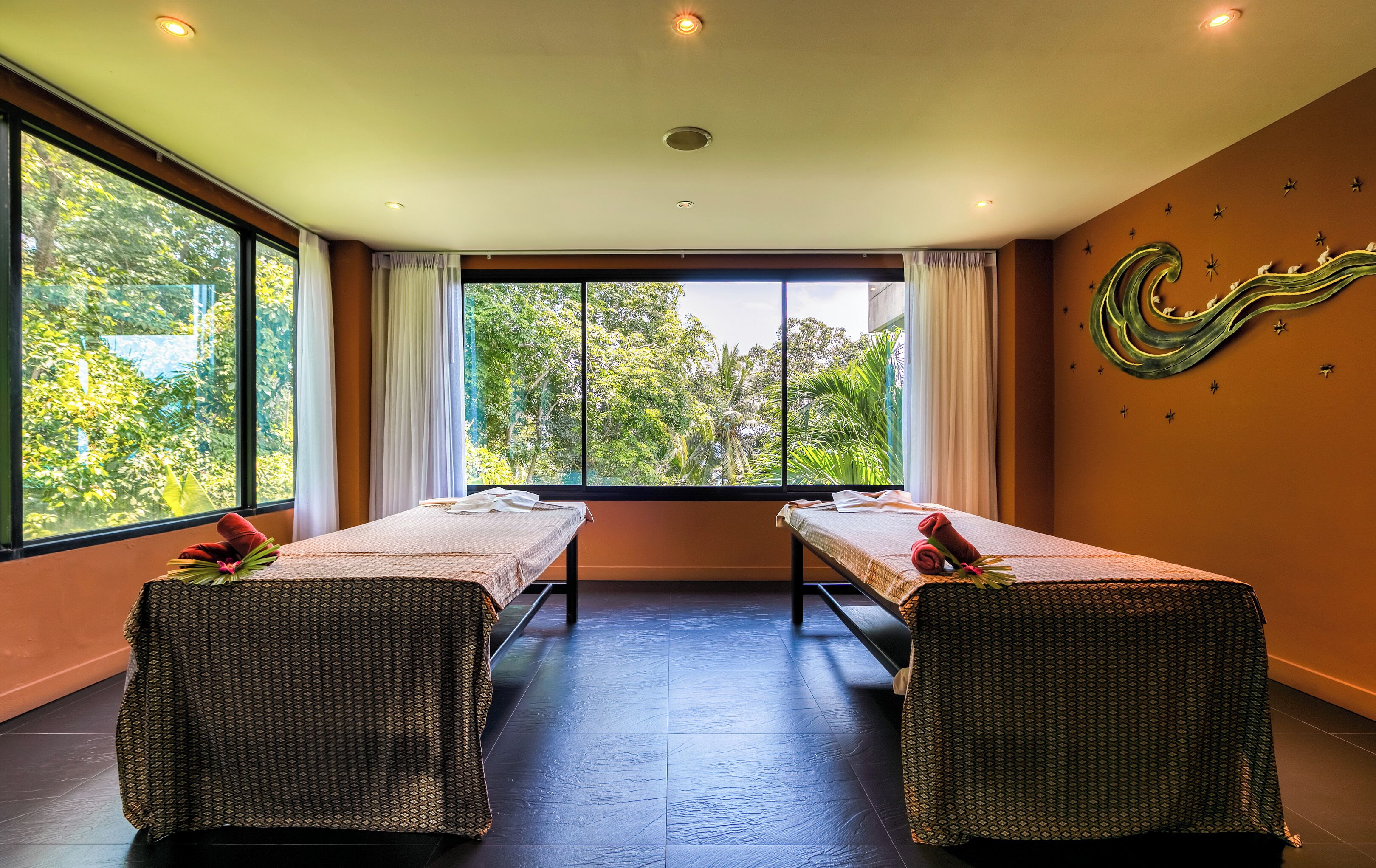 A room with two massage tables, large windows, and a view of greenery.