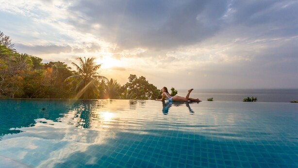 En person som kopplar av vid en infinitypool med utsikt över havet och palmerna.