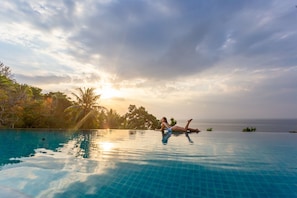 Una persona descansando en una piscina infinita con vista al océano y palmeras.