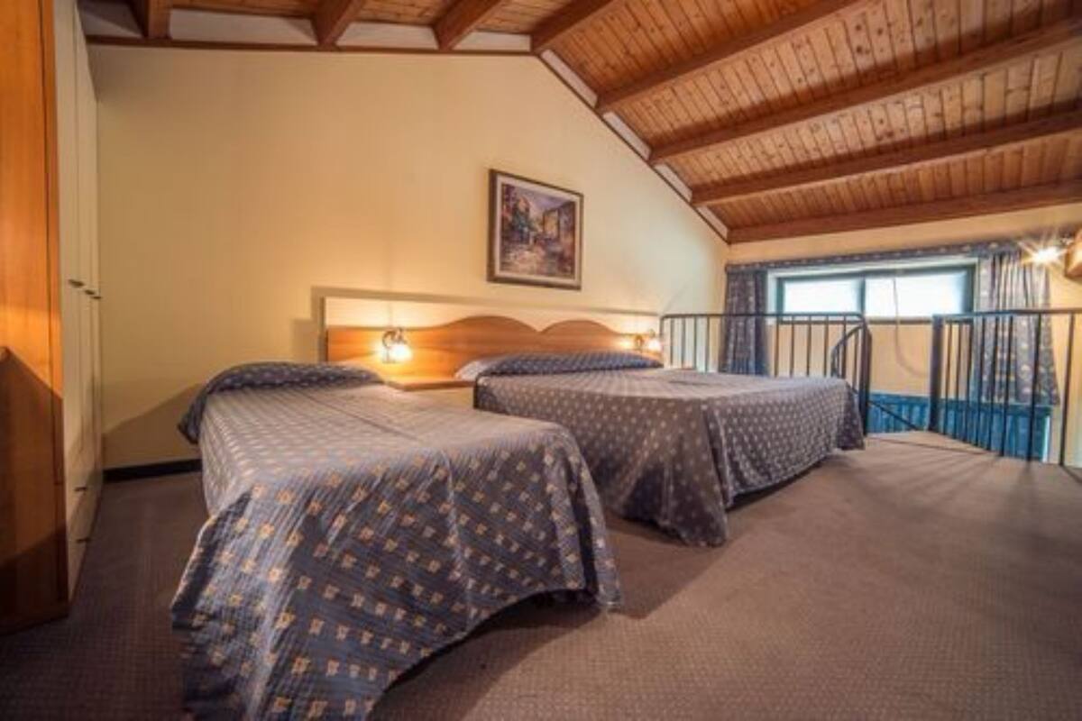 A room with two beds, wooden ceiling beams, a painting on the wall, and a balcony with a railing.