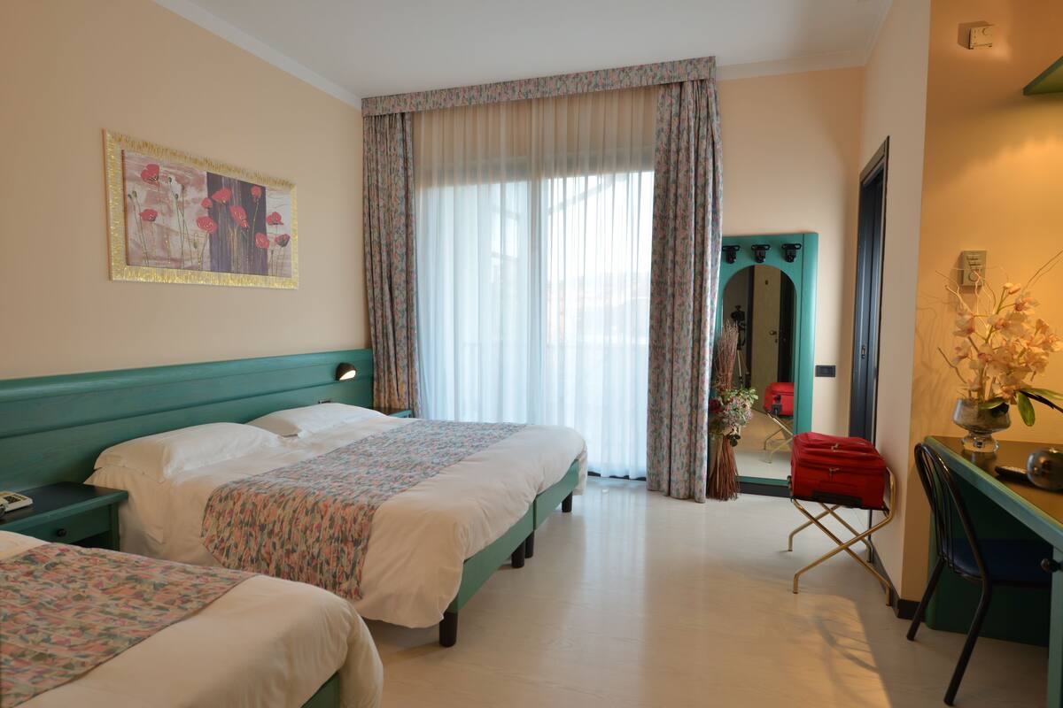A hotel room with two beds, a desk, a chair, and a large window with curtains.