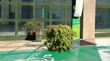 A green bike parking area with a sign for e-Station, a potted plant, and a building with large windows in the background.