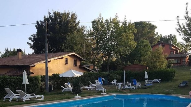 A swimming pool with lounge chairs and umbrellas, surrounded by greenery and houses. - Maya (Zagarolo)