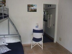A bedroom with a bunk bed, a small desk, and a shower area.