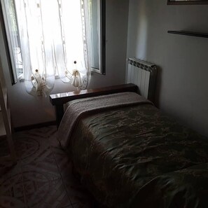 A bedroom with a bed, a radiator, a window with curtains, and a patterned floor.