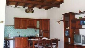 A kitchen with wooden cabinets, a dining table, chairs, a television, and a ceiling with exposed beams. - Maya (Zagarolo)