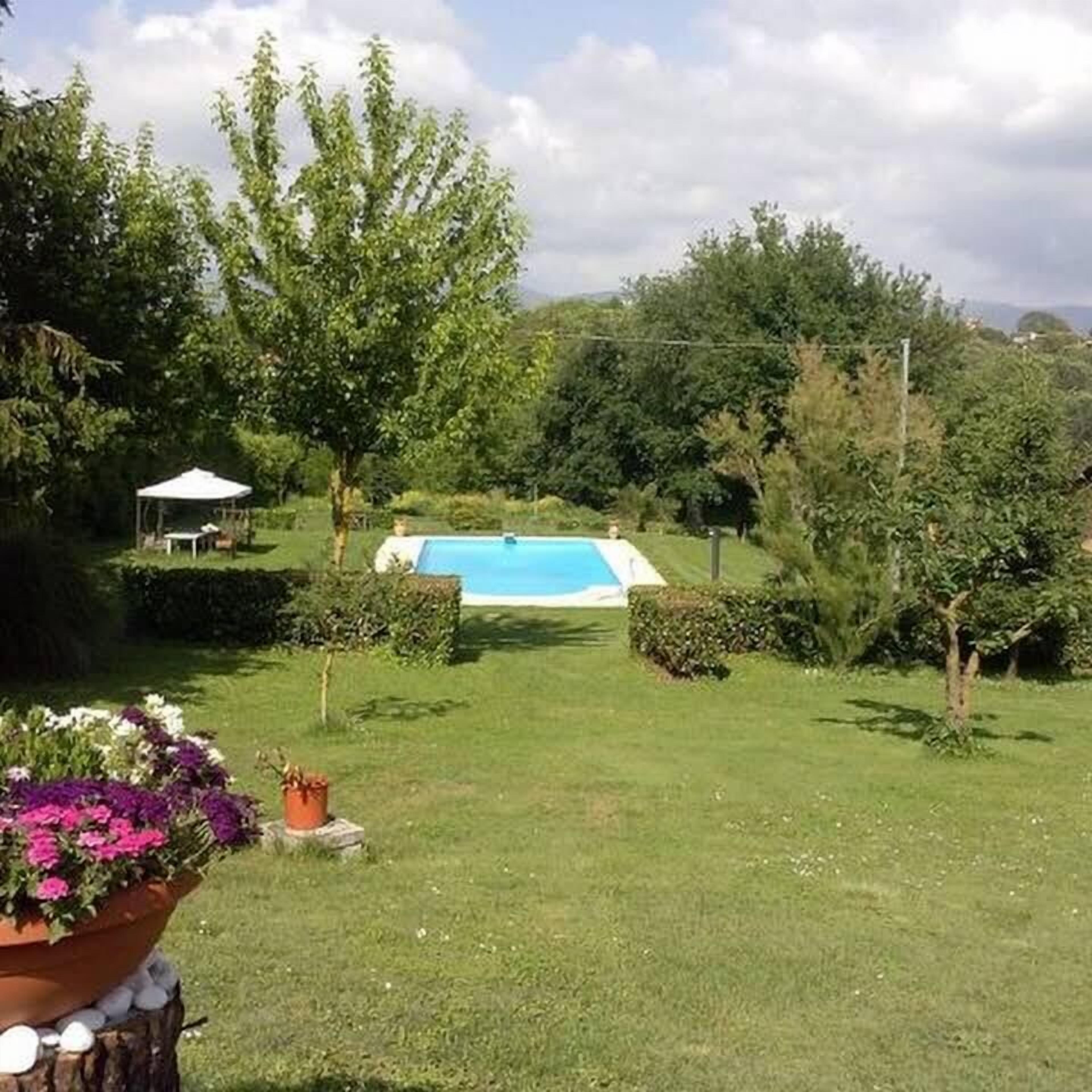 Un jardin à l’arrière de la maison, avec une piscine, entouré d’arbres et agrémenté d’un potager.