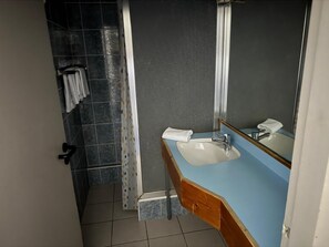 A bathroom with a blue countertop, a white sink, a mirror, and a shower area with a curtain. - Hotel Dupleix (Quimper)