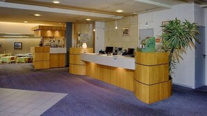 A reception area with a wooden reception desk, a large potted plant, and a seating area with tables and chairs. - Hotel Dupleix (Quimper)