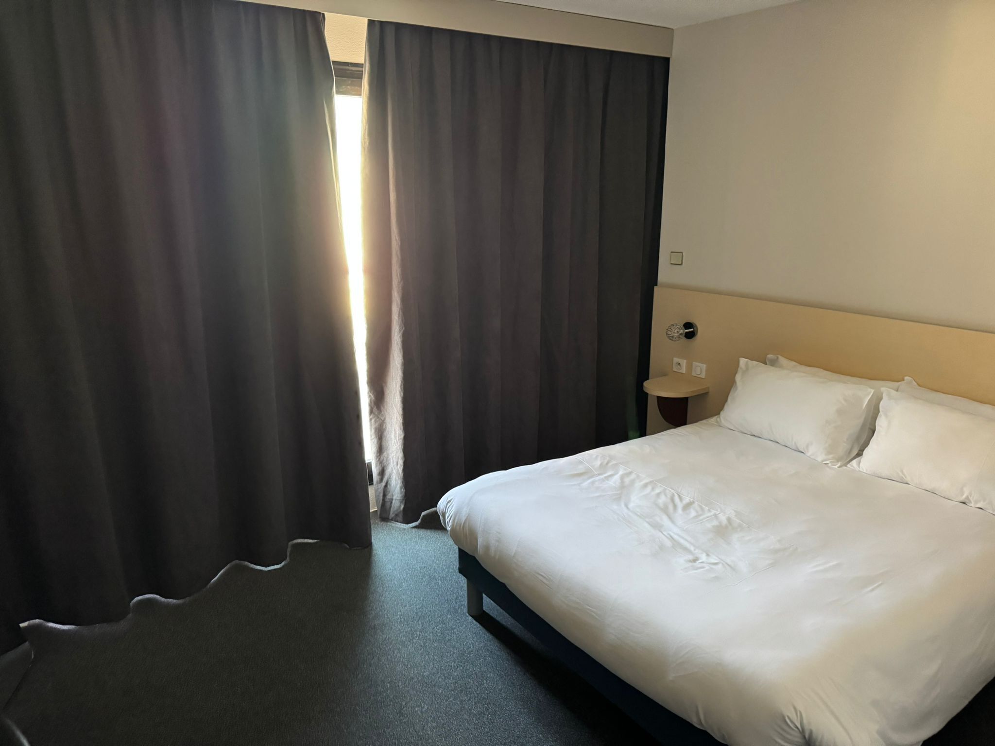 Ein Hotelzimmer mit einem großen Bett, einem Nachttisch und einem Fenster mit Vorhängen.