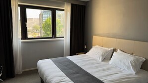 A hotel room with a large bed, a window with curtains, and a view of buildings outside. - Hotel Dupleix (Quimper)