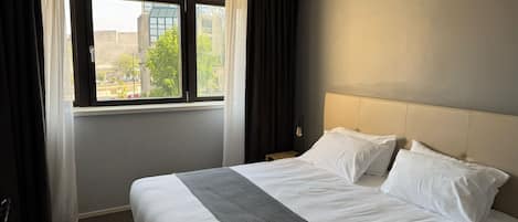Una habitación de hotel con una cama grande, una ventana con cortinas y vistas a edificios.