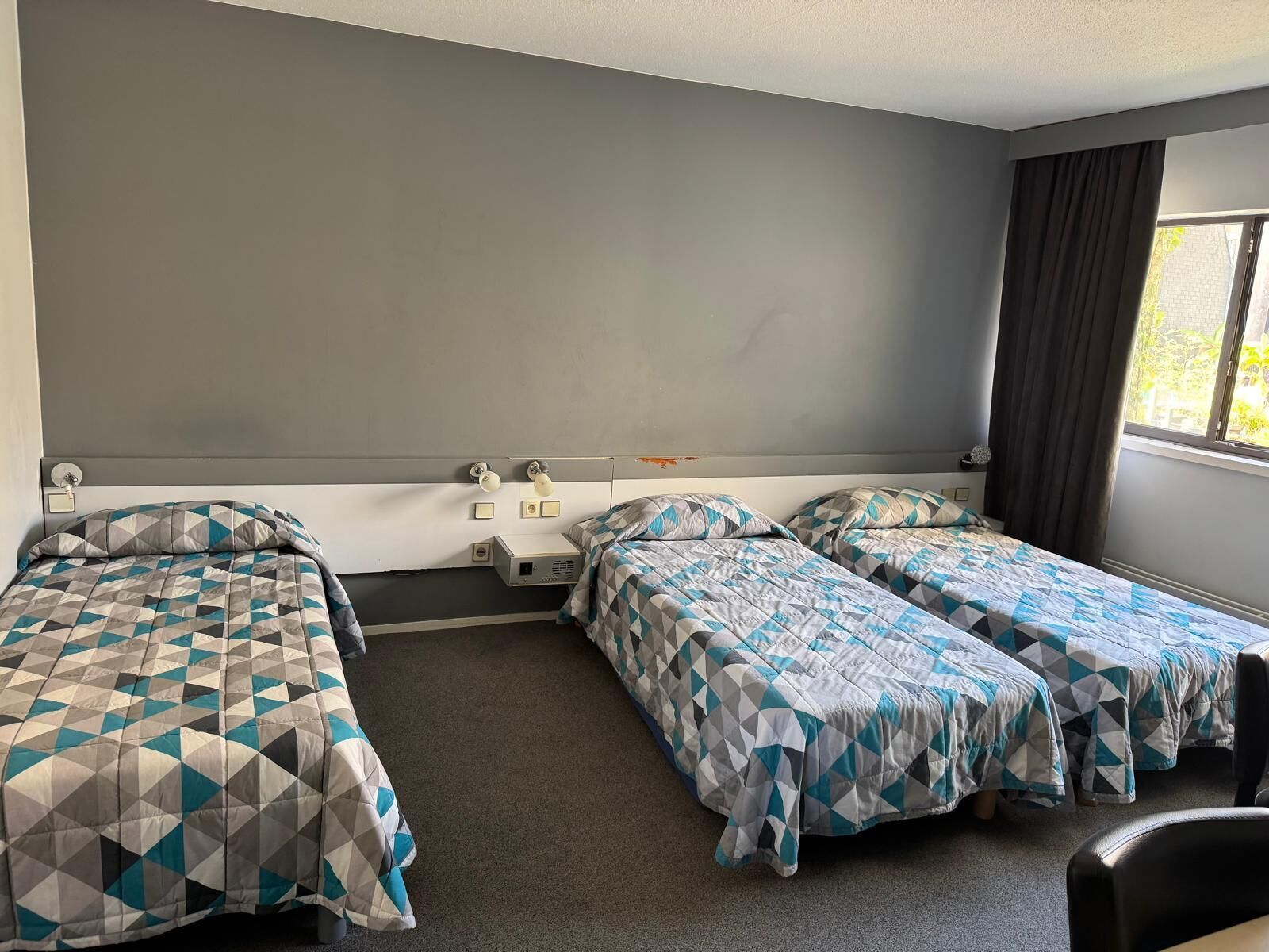 Een kamer met twee enkele bedden, een klein bureau, een stoel en een raam met gordijnen.