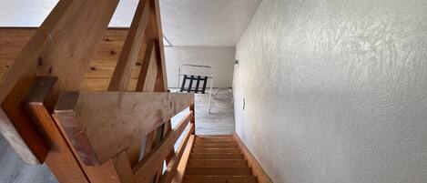 Una escalera de madera que conduce a una habitación con pared blanca y una silla de metal.