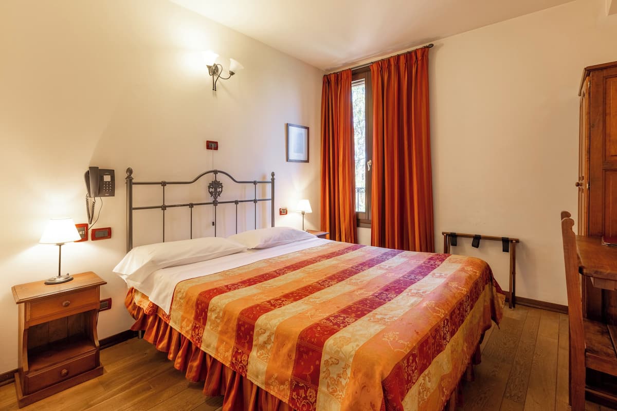 Un dormitorio con cama, lámparas de noche, mesita de noche, ventana con cortinas y un armario de madera.