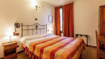 Un dormitorio con cama, lámparas de noche, mesita de noche, ventana con cortinas y un armario de madera.