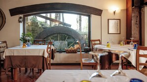 A restaurant with tables set for dining, a large arched window, and a stone wall visible through the window. - Locanda del Mulino (Maranello)