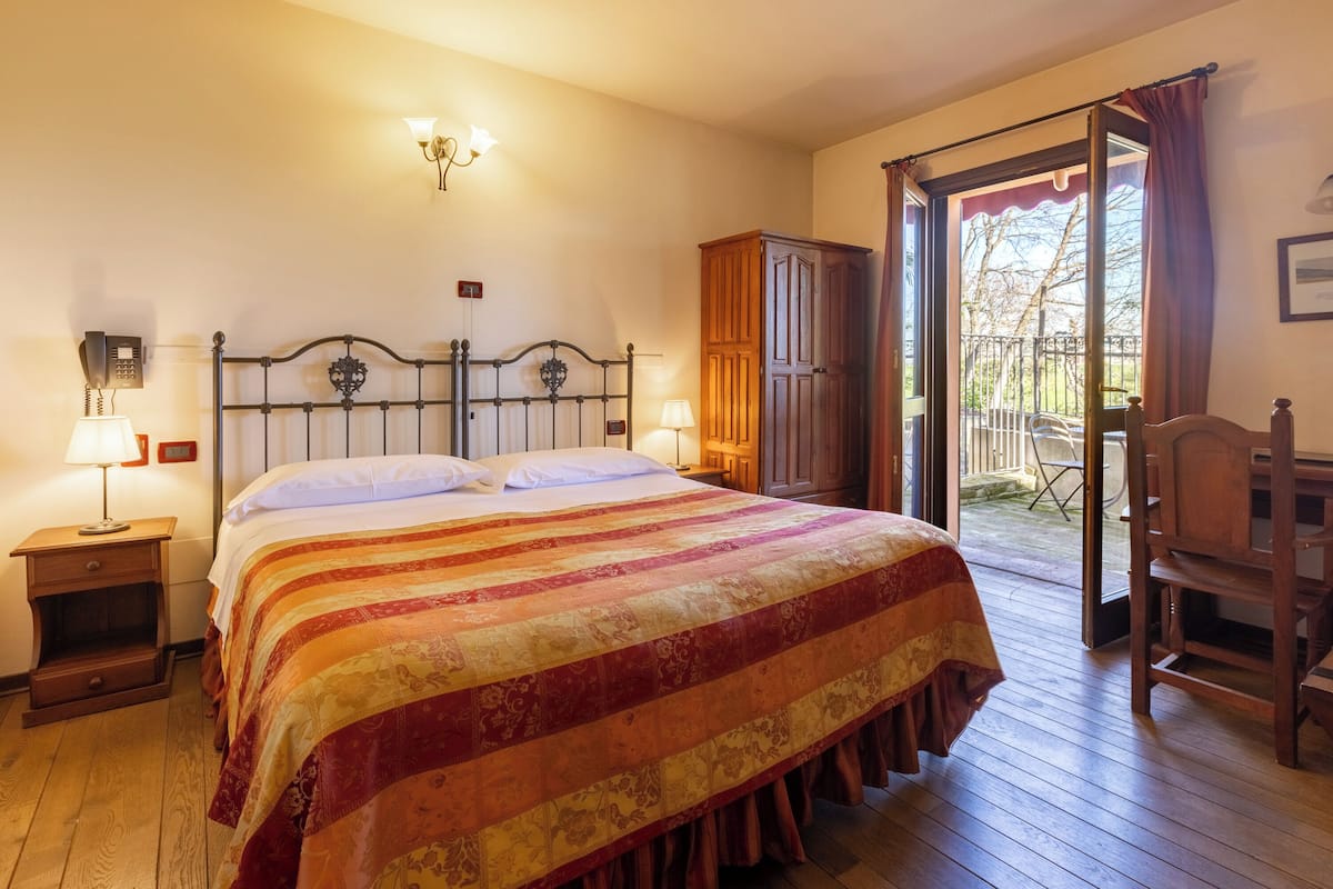 Un dormitorio con cama, lámparas de noche, armario y balcón con una silla.