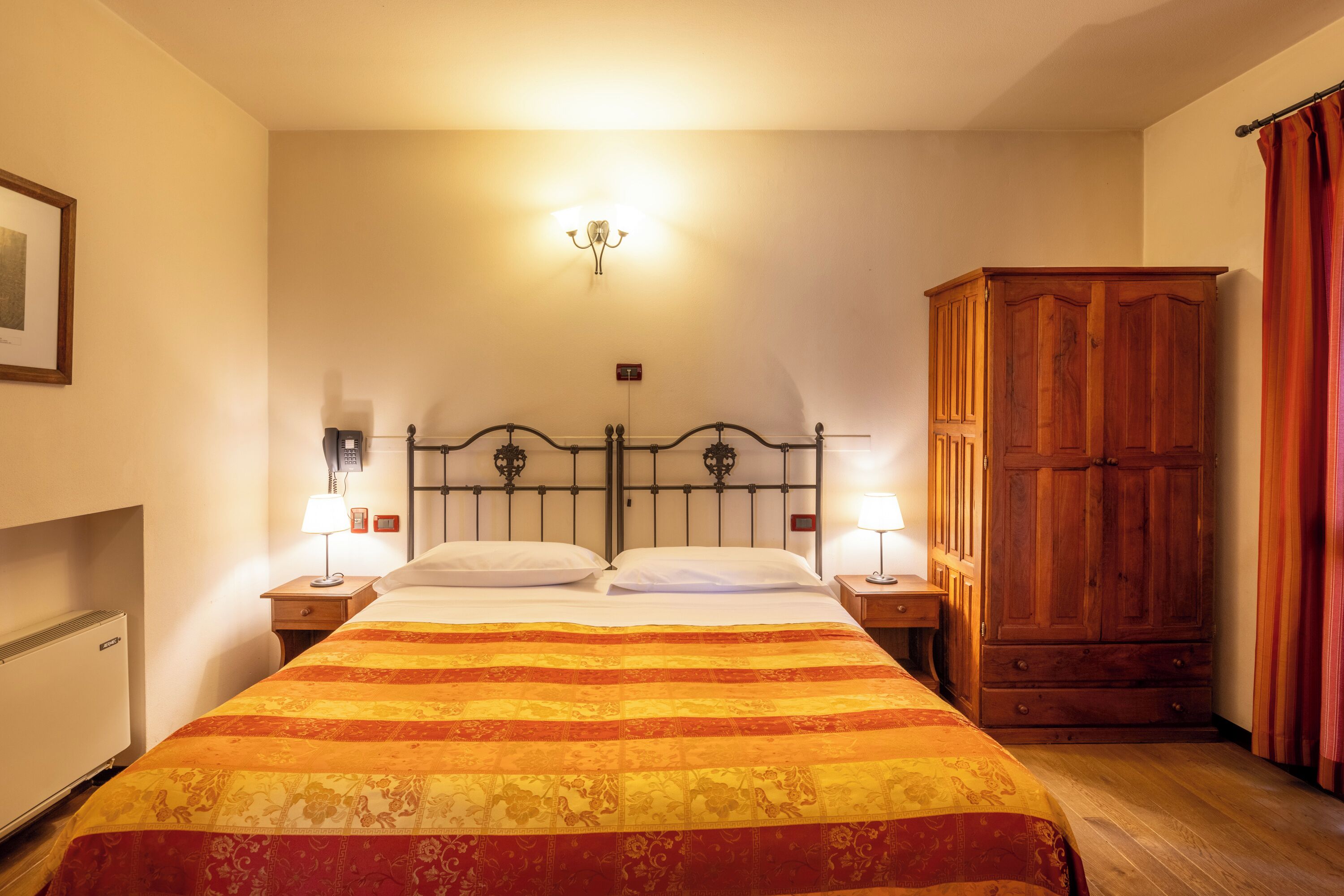Habitación de hotel con cama, dos lámparas de noche, armario de madera y aplique de pared.