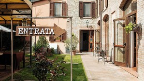 A courtyard with a sign reading 'ENTRATA,' a brick building with arched windows, and a covered seating area. - Locanda del Mulino (Maranello)