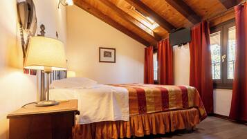 A bedroom with a wooden ceiling, a bed with a patterned bedspread, a bedside lamp, and a window with curtains.