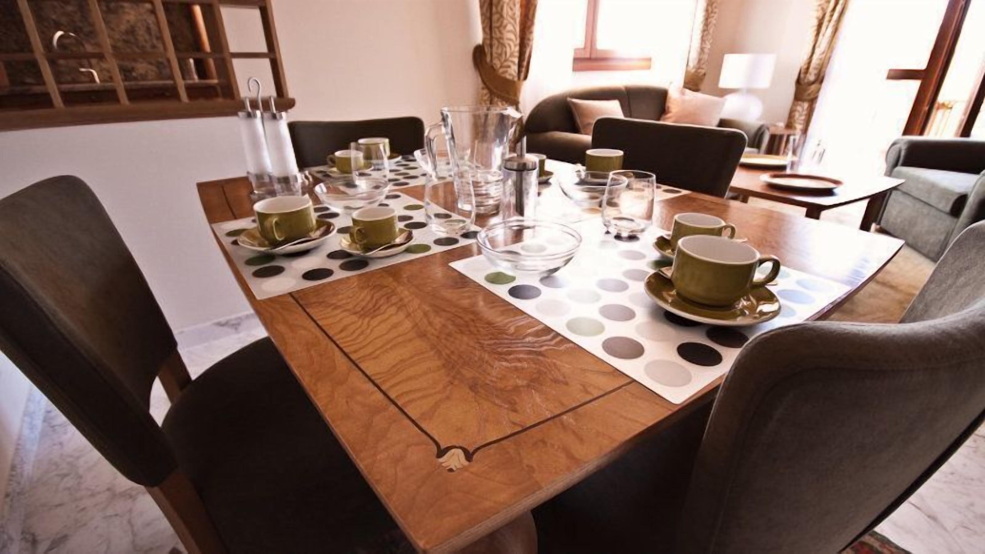 Una mesa de comedor dispuesta con varias tazas y platillos, una jarra y un jarrito de vidrio.