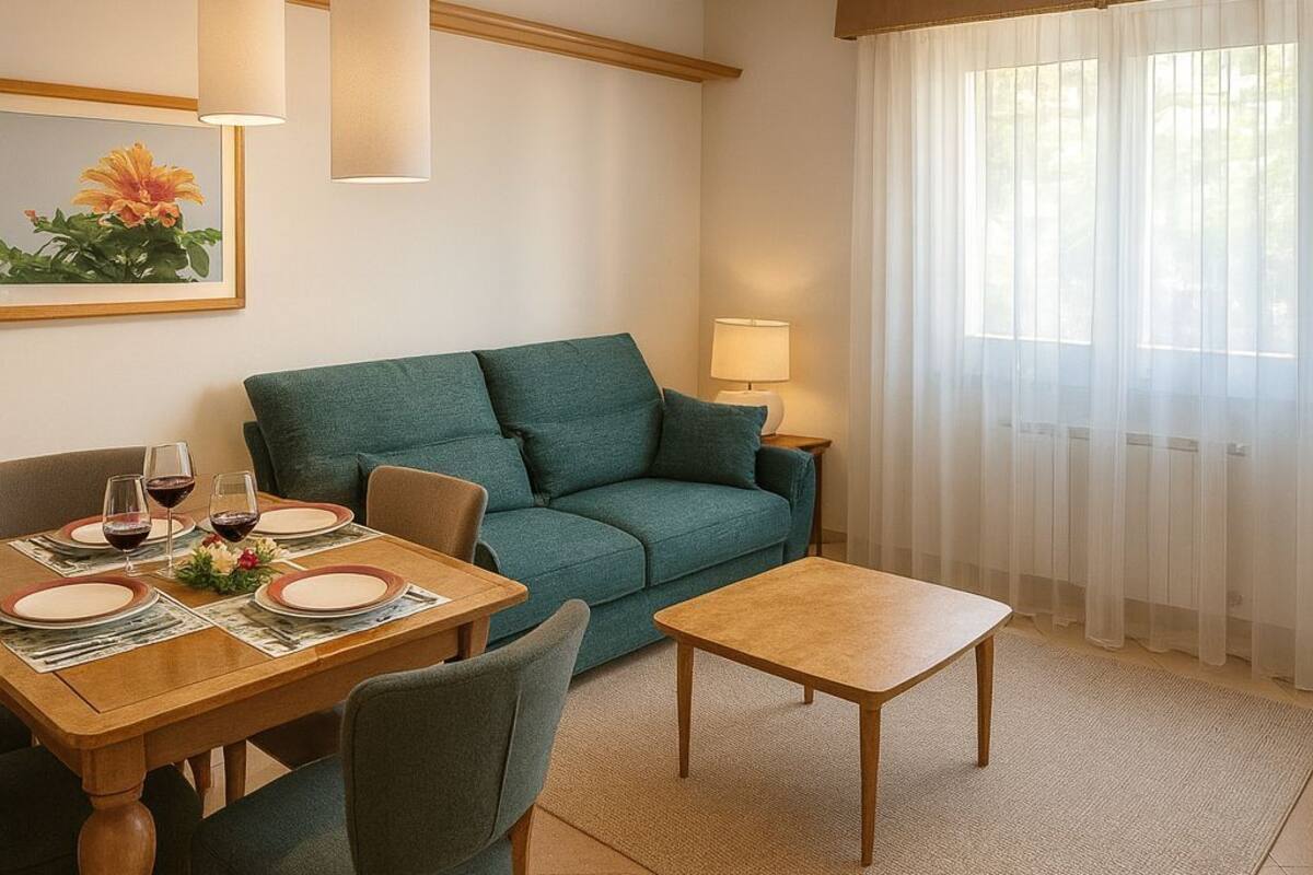 Una sala de estar con un sofá verde, una mesa de centro de madera, una mesa de comedor con platos y vasos, y una lámpara sobre una mesita auxiliar.