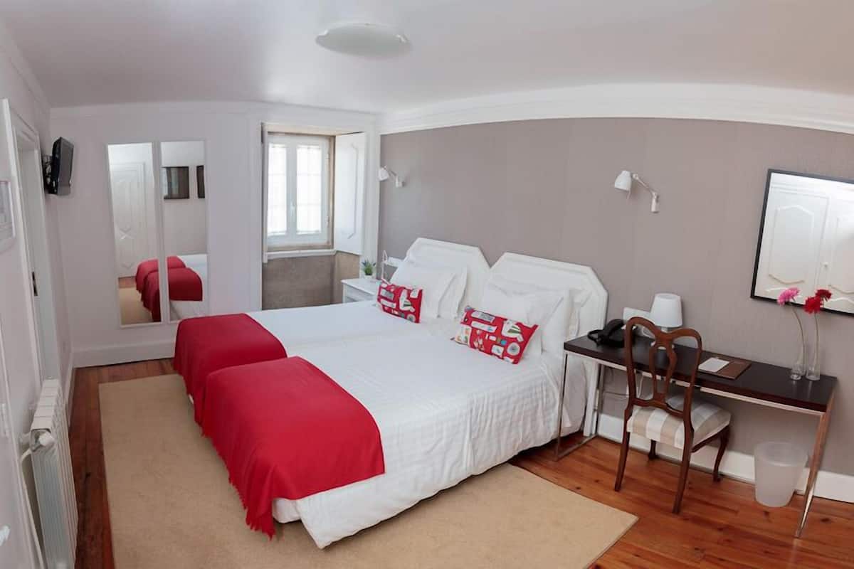 A bedroom with a large bed, a desk, and a chair. There is a mirror on the wall and a window with curtains.