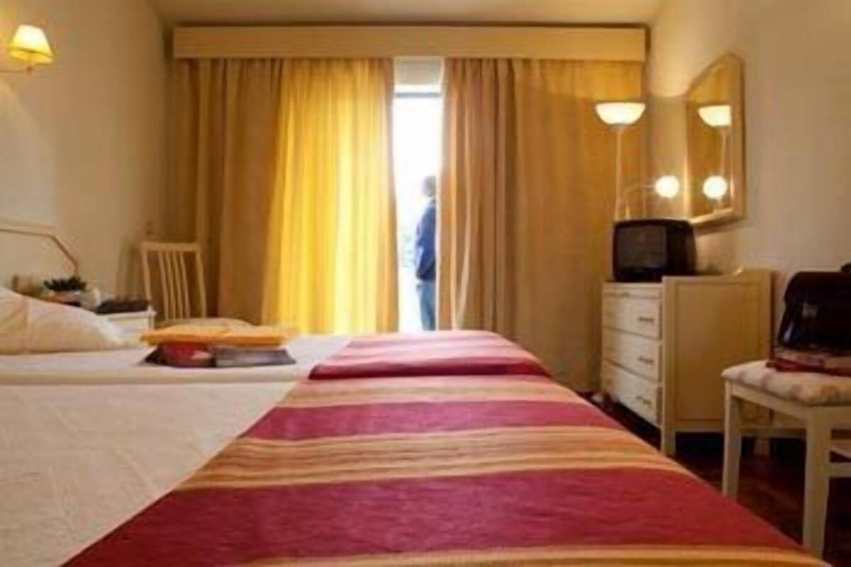 A hotel room with a bed, a desk, a chair, a television, and a window with curtains.